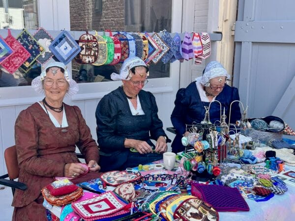 Drie vrouwen in klederdracht haken zwijgend voor een historisch pand in De Waal op Texel.